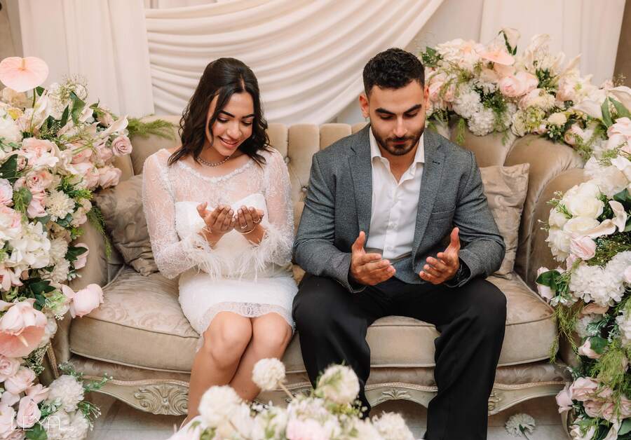 Ahmed and Nada seated together, hands raised in prayer